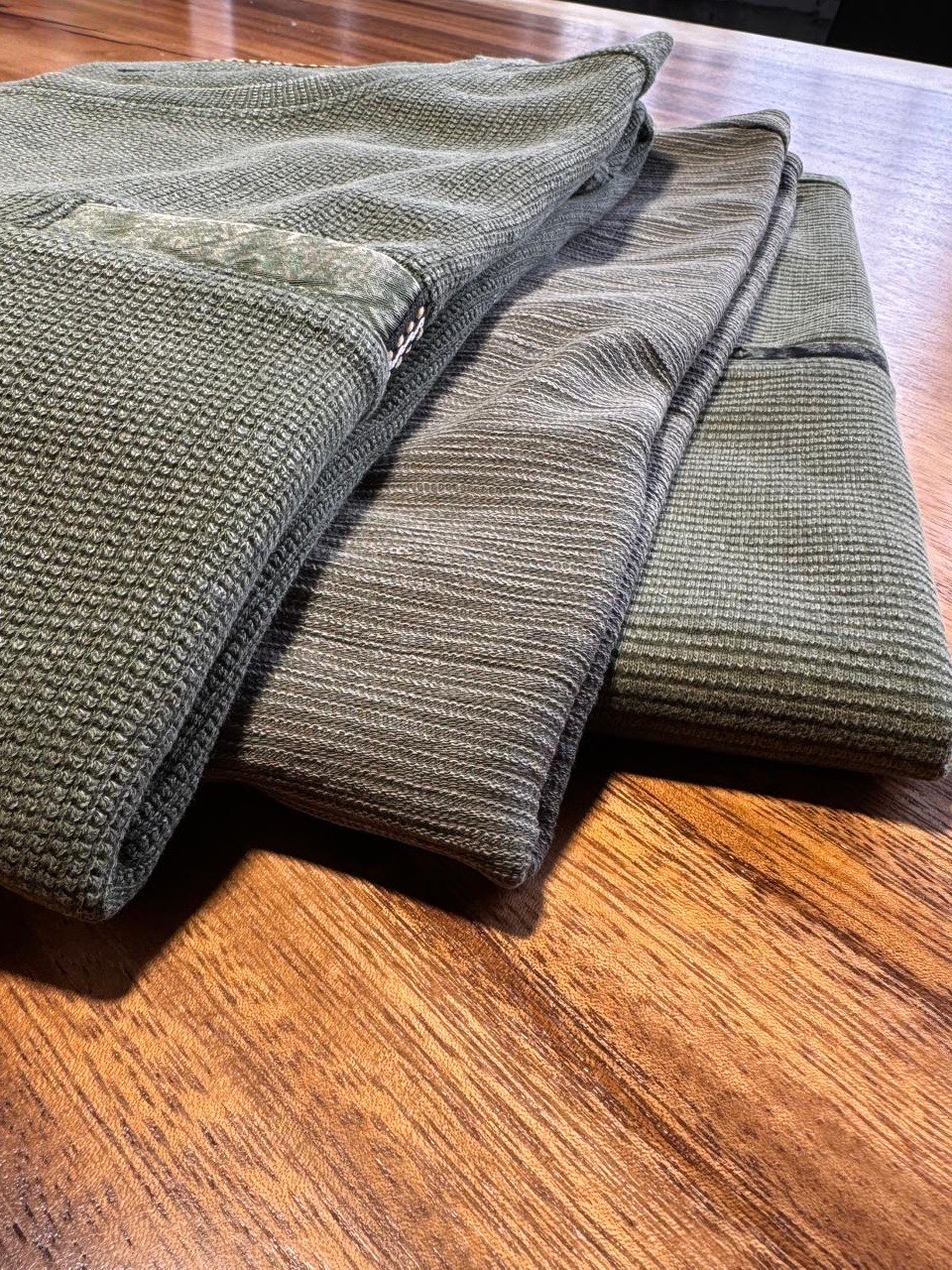 Gefaltete Strickteile in Oliv auf einem Holztisch